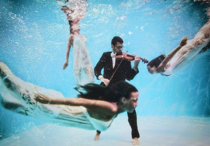 Violinist plays the violin under water with girls