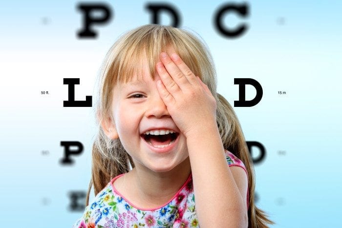 A child is laughing while blocking one of her eyes.