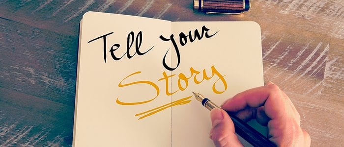 Hand writing "tell your story" in a book