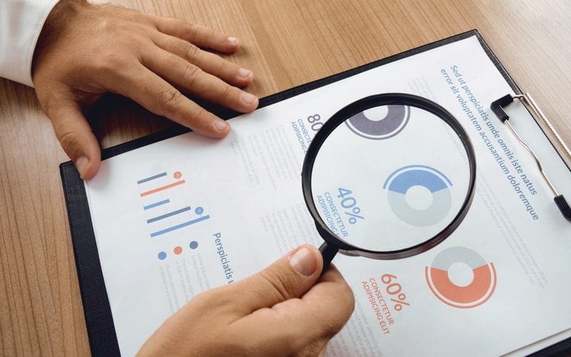 Market research. Businessman hand holding magnifier and closer study report from market research.